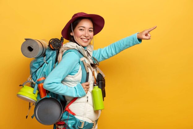 Glad smiling hiker dressed casually, stands with backpack against yellow background Image by wayhomestudio on Freepik